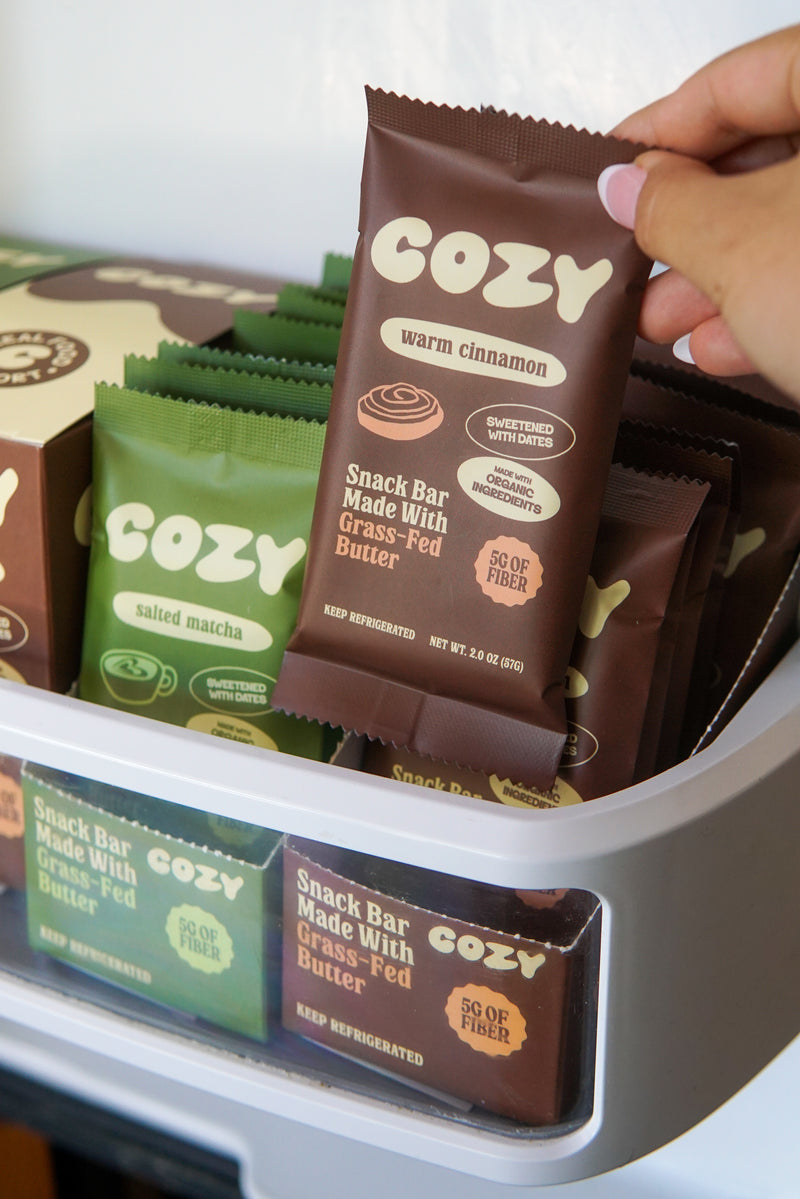 Holding a COZY Warm Cinnamon bar at the open fridge