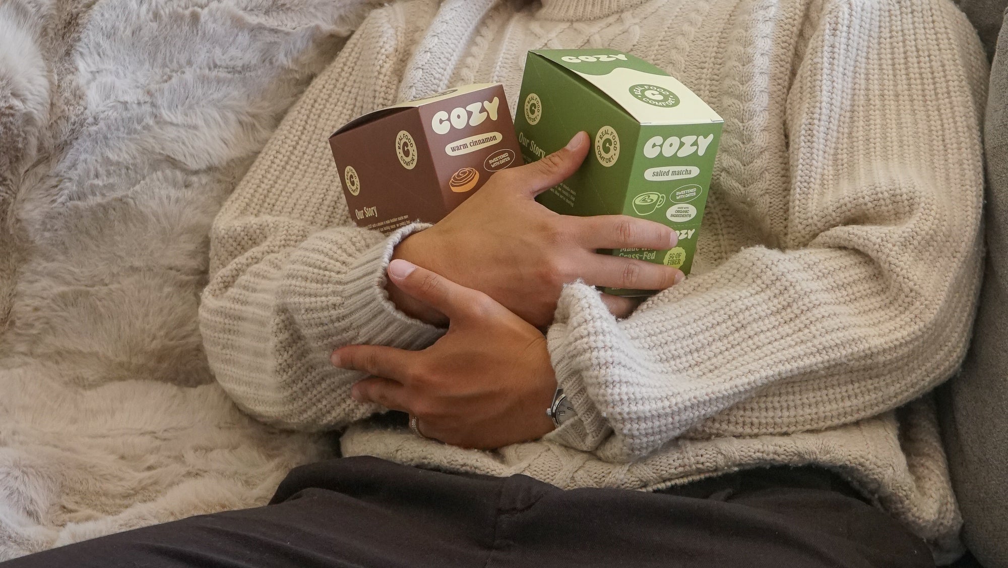 Person on a sofa hugging boxes of COZY snack bars