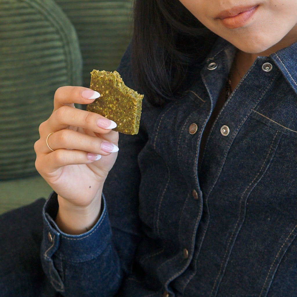 Person on a green sofa eating a COZY Salted Matcha refrigerated snack bar